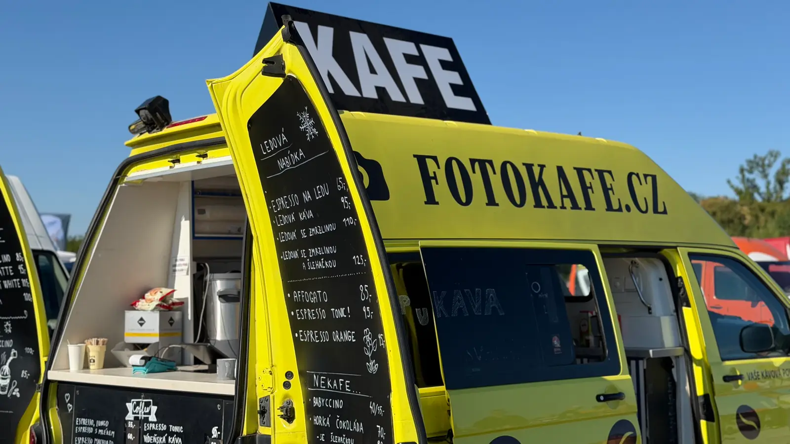 Žlutá dodávka s kávou otevřená pro návštěvníky, na střeše cedule KAFE
