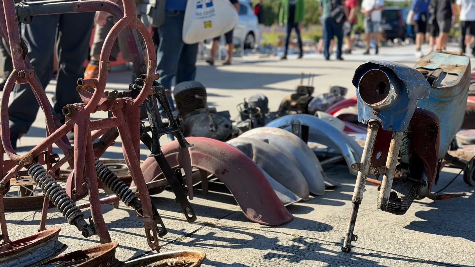 Rámy motocyklů, blatníky a modrá kapotáž skútru rozložené na ploše